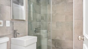 Ein modernes Badezimmer mit Duschabtrennung aus Glas, einem weißen Waschbecken und einem Spiegel darüber.