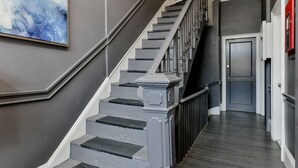 Eine Treppe mit Handlauf, einer Tür am Fußende und einer Wandleuchte.