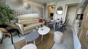 A modern living room with a sofa, a dining table, and chairs. There is a plant and a mirror on the wall.