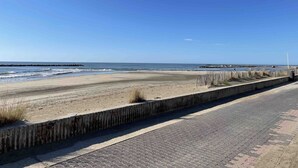 A beach with a paved walkway and wooden fence.