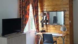 A room with a wooden wall, a television on a cabinet, a desk with a chair, a mirror, and a window with curtains. - Vigets Balou (Fort-de-France)