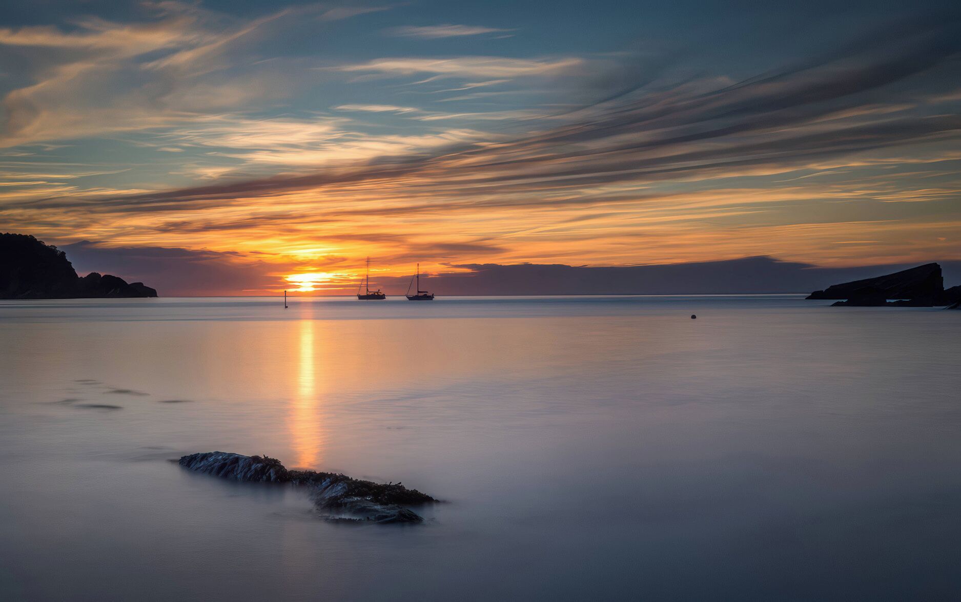 Rustig water dat de zonsondergang weerspiegelt, een zeilboot en verre landschappen.
