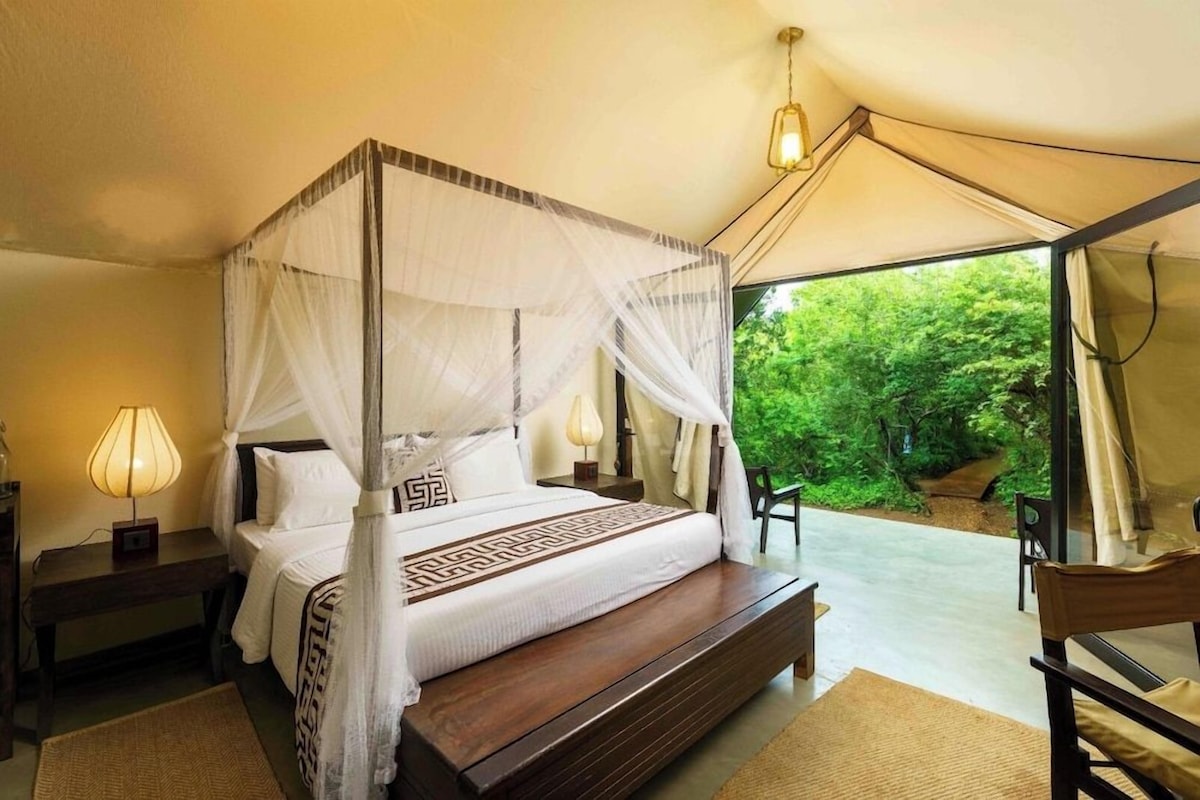 A four-poster bed with a canopy, bedside lamps, and a view of greenery outside.