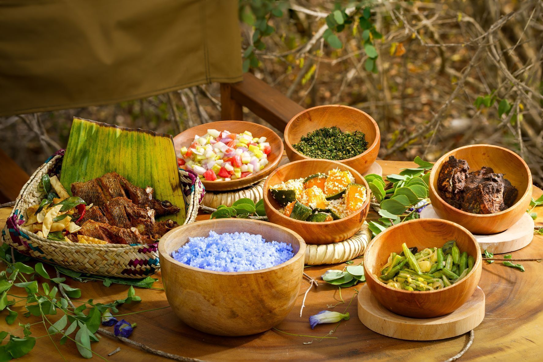Une variété d’aliments est présentée sur une table en bois, à l’extérieur.