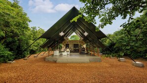 A covered outdoor seating area with a concrete floor, surrounded by trees and a clear sky. - Makini Bush Camp (Kataragama)