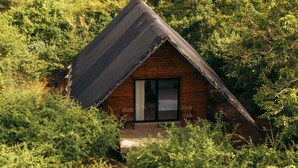 A cabin nestled in a forest, with a sloped roof and a visible door. - Makini Bush Camp (Kataragama)