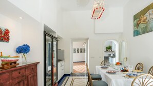 Un coin repas avec une table blanche dressée pour quatre personnes, des chaises en bois, un sol à motifs et une vue sur la cuisine.