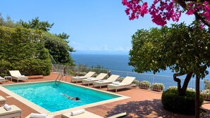 Un espace piscine comprenant des chaises longues, une piscine et une vue sur la mer.