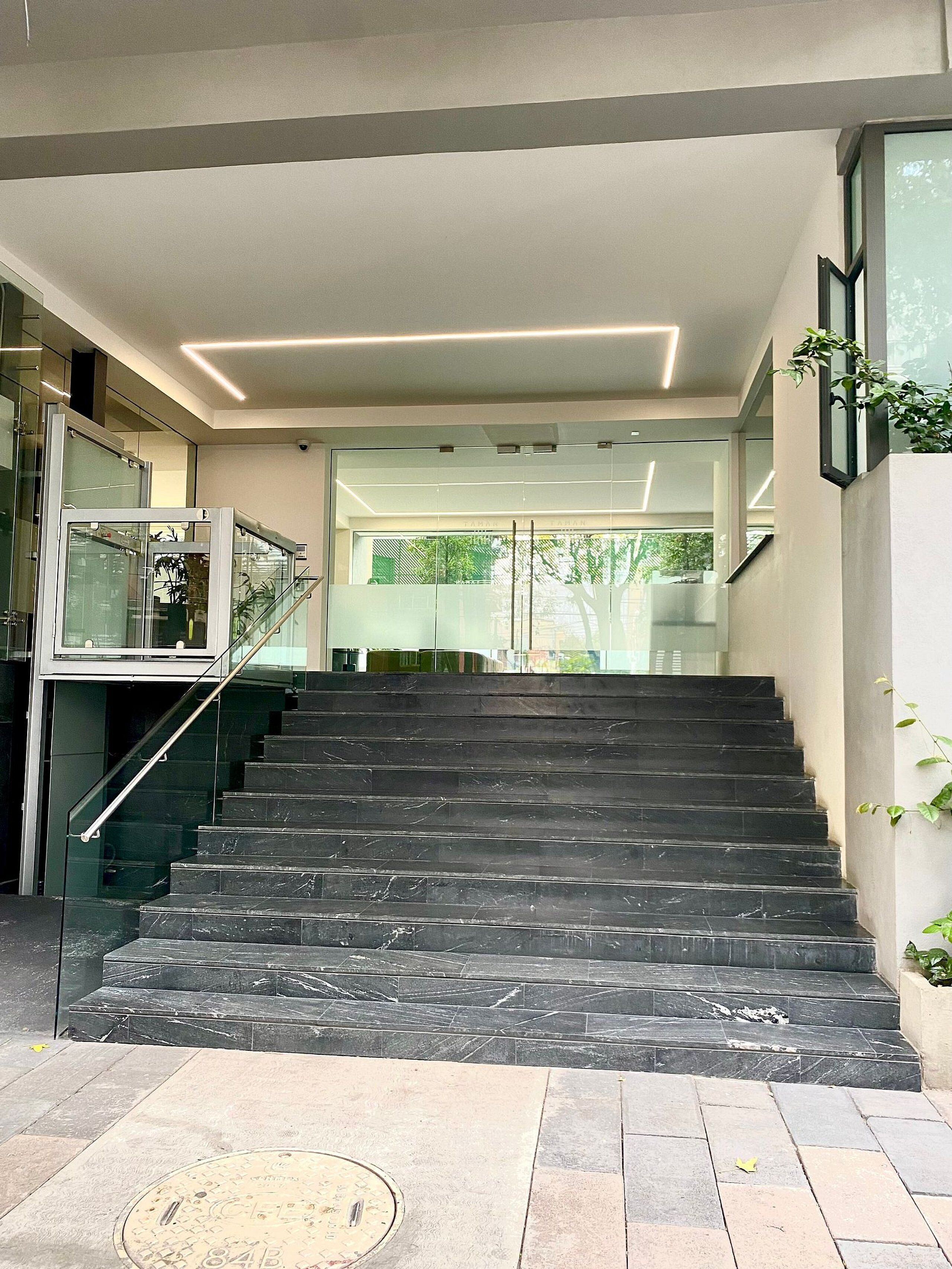 A modern staircase with glass railings and a metal handrail leading to a glass door entrance.