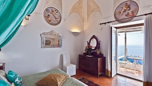 A bedroom with a bed, a dresser, a mirror, and a view of the sea through a glass door.