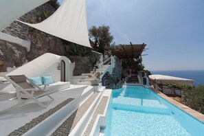 A poolside area with a clear view of the sea, a white outdoor seating area, and a stone wall.