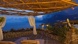 A covered outdoor seating area with stone walls and a view of the sea.