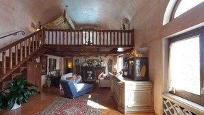 A spacious living room with a high ceiling, a wooden staircase, and a large window.