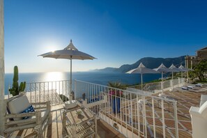 A balcony with a view of the sea, white umbrellas, and lounge chairs.
