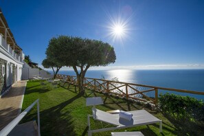 A seaside property with a wooden deck, lounge chairs, and a view of the ocean.