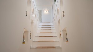 Una escalera de paredes blancas y peldaños de madera que conduce a una plataforma con una lámpara.