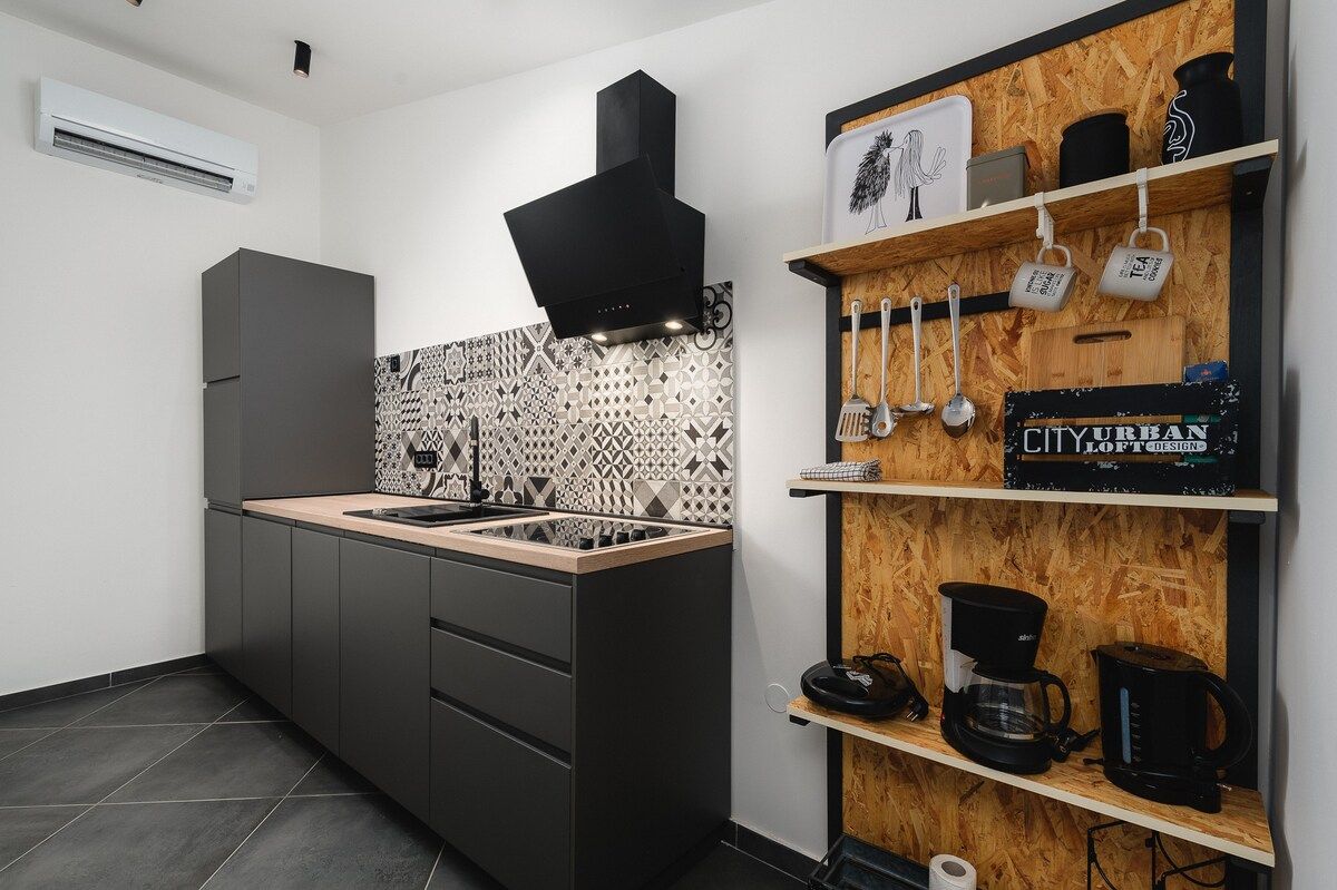 Una cocina moderna con estufa integrada, campana extractora negra y repisa de madera con utensilios de cocina.