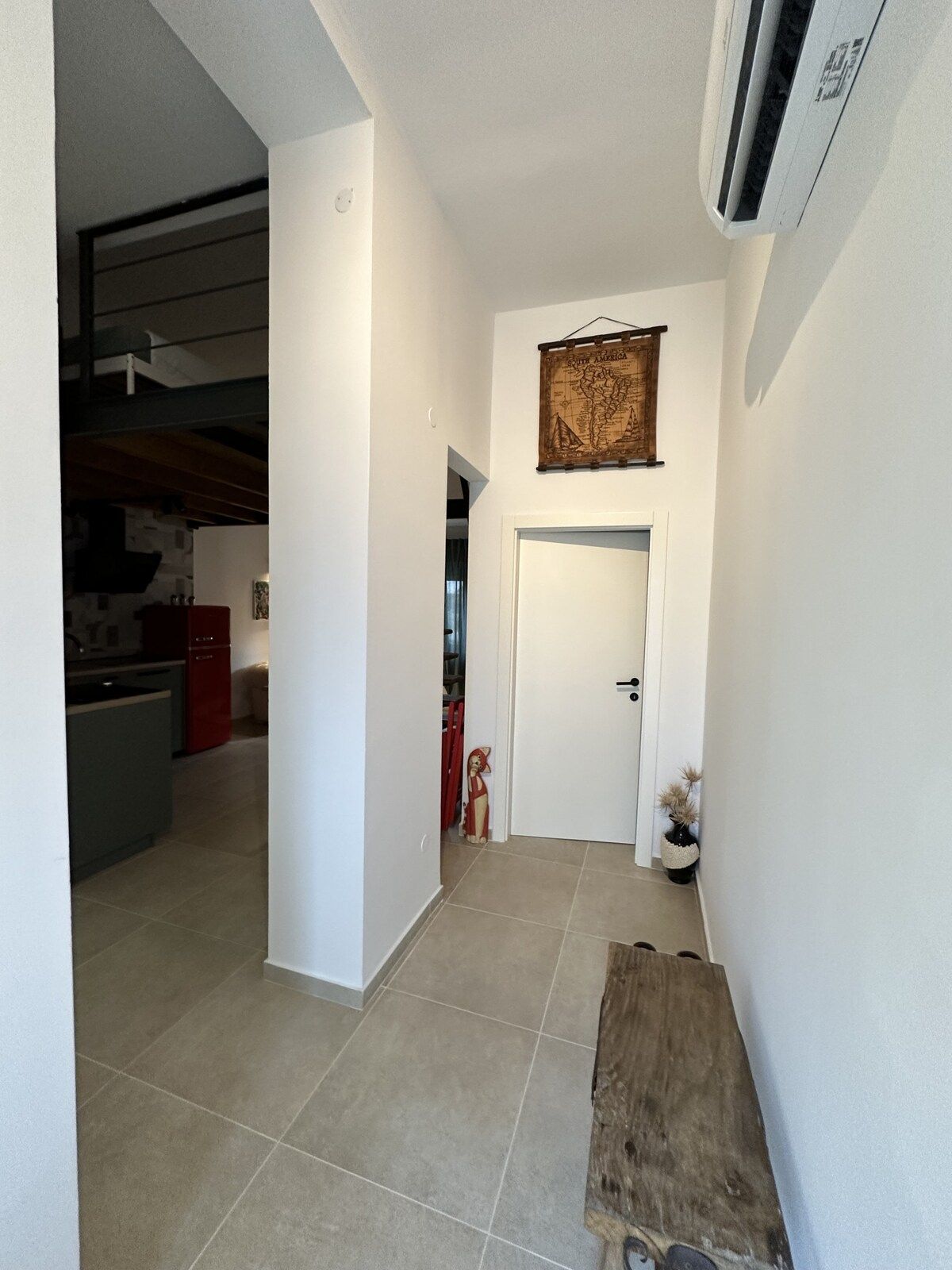 Un pasillo con un banco de madera, una puerta blanca y un mapa en la pared.