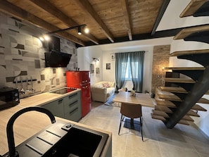 A modern kitchen with a built-in stove, a red refrigerator, and a dining area with a wooden table and chairs. - Apartment Urban Green (Porec)