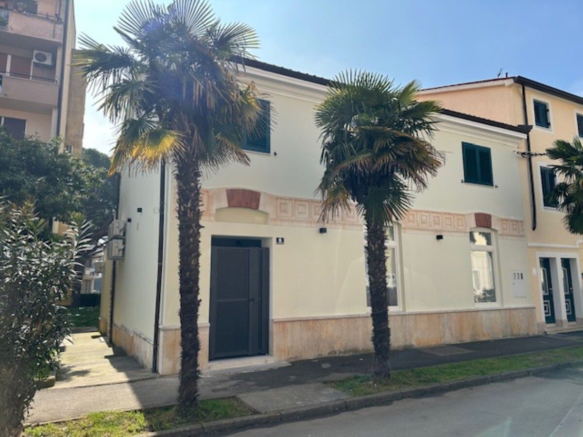 Ein zweistöckiges Gebäude mit einer beigen Fassade, einer schwarzen Tür und einem kleinen Balkon.