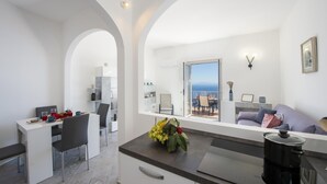 A modern kitchen with a dining area, a view of the sea, and a cozy living space with a sofa and a coffee machine. - Villa Ecuba - Villa for Groups in a Strategic Position (Praiano)