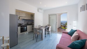A modern kitchen with a dining area, a sofa, and a sliding glass door leading to a balcony. - Villa Ecuba - Villa for Groups in a Strategic Position (Praiano)