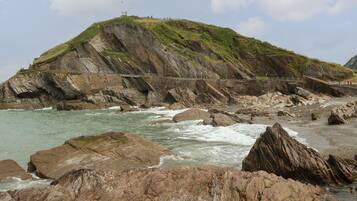 A rocky coastline with a bridge and a hill with a flag.