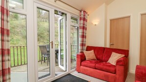 A room with a red sofa, a wooden door, and a glass door leading to an outdoor area with a table and chairs. - 7 Manleigh Park (Ilfracombe)