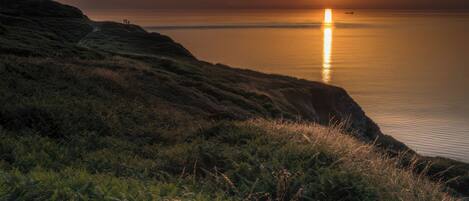 A coastal landscape with a sunset, cliffs, and a calm sea.