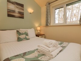 Una cama bien hecha con una colcha de estampado floral, un almohadón con diseño de hojas y una ventana con vistas a árboles.