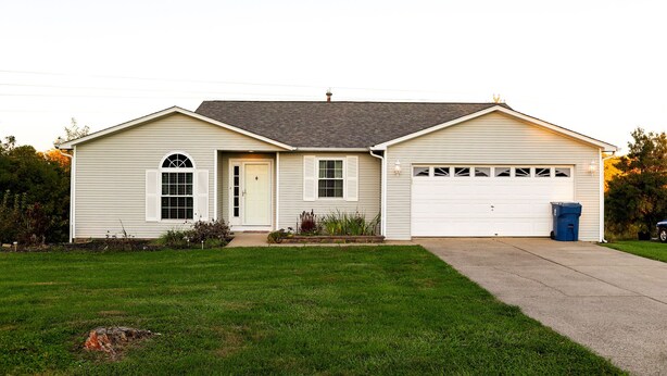 Une maison de plain-pied avec un garage, une porte d’entrée et un petit jardin devant.