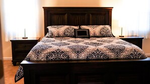 Une chambre à coucher avec un grand lit, une tête de lit en bois foncé, une literie à motifs, deux tables de chevet et des rideaux.