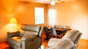 Un salon comprenant un canapé, un fauteuil inclinable, une table à manger avec des chaises, une lampe et un ventilateur de plafond.