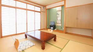 Een traditionele Japanse kamer met tatami vloerbedekking, een houten tafel, een televisie en een kast.