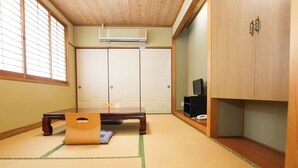 Een traditionele Japanse kamer met tatami vloerbedekking, een lage tafel, een televisie en schuifdeuren.