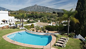 Ein Pool mit Bergblick, umgeben von einer gepflegten Rasenfläche und einigen Liegestühlen.