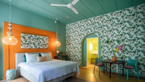 Une chambre à coucher avec un lit, deux lampes suspendues, une petite table avec des chaises et une salle de bain visible à travers une arche.
