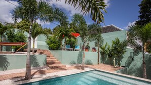 Une piscine entourée de palmiers et un bâtiment verdoyant surmonté d’un toit rouge.