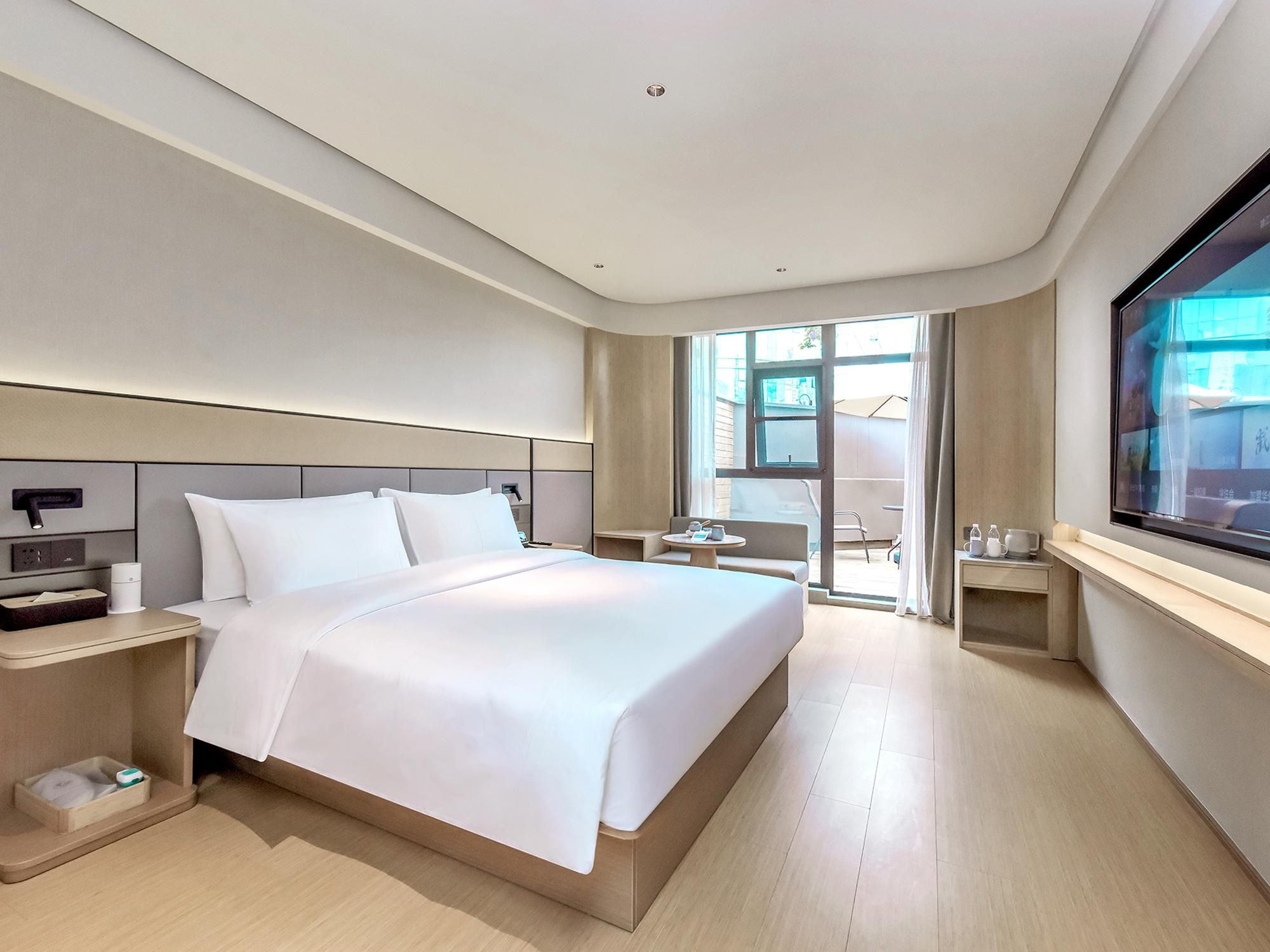 A modern hotel room with a large bed, bedside tables, a TV, and a view of the outdoors.