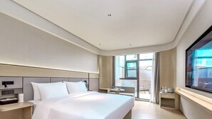 Una habitación de hotel moderna con una cama grande, mesitas de noche, un televisor y un balcón con mobiliario exterior.