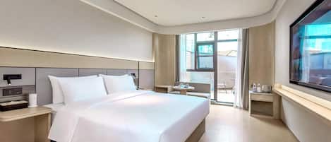 A modern hotel room with a large bed, bedside tables, a TV, and a view of the outdoors.