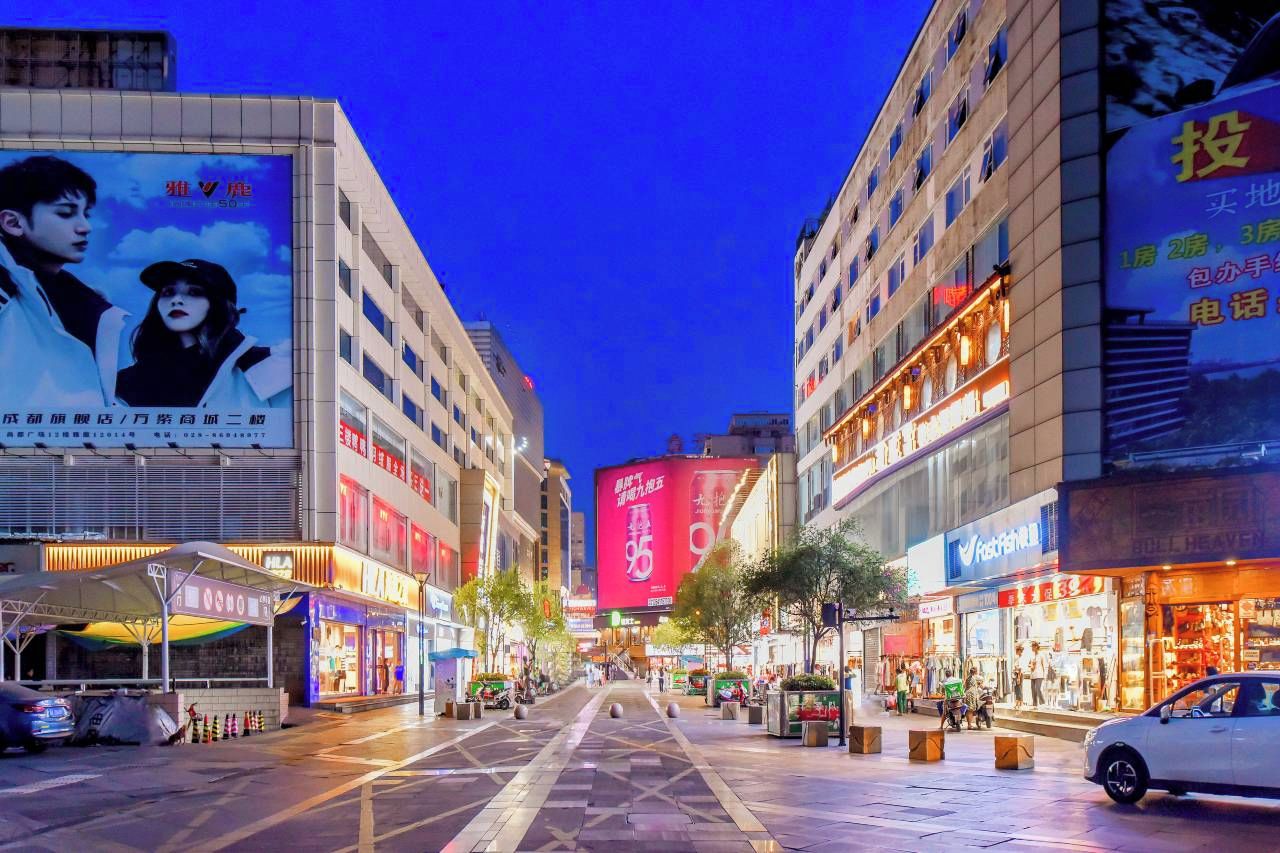 A city street at night with illuminated billboards and storefronts.