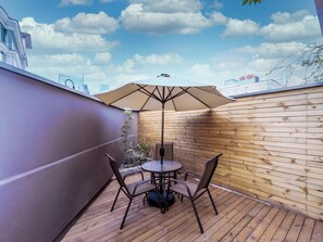 Une terrasse en bois avec une table ronde et des chaises, un parasol et une vue sur la ville.