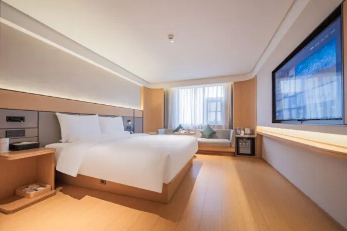 A modern hotel room with a large bed, a TV mounted on the wall, a sofa, and a small table.