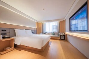 Une chambre d’hôtel moderne avec un grand lit, un téléviseur fixé au mur, un canapé et une petite table.