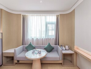 A modern hotel room with a sofa, a coffee table, and a side table with a kettle and cups. - Ji Hotel (Chengdu)