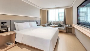 Una habitación de hotel moderna con una cama grande, un área de descanso con una mesa y un ventanal amplio.