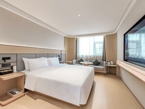 Une chambre d’hôtel moderne avec un grand lit, un coin salon avec une table et une grande fenêtre.