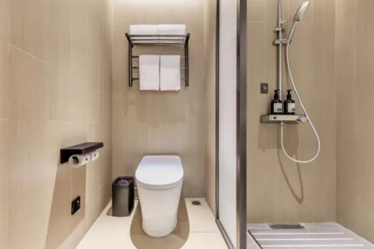 A modern bathroom with a toilet, a towel rack, a shower, and a small trash bin.