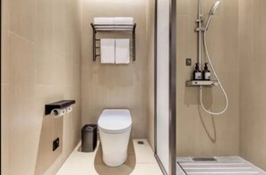 Un baño moderno con inodoro, toallero, ducha y un pequeño cubo de basura.